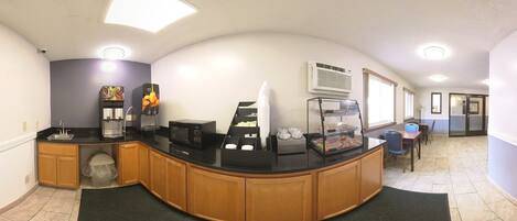 A clean, modern kitchen with a curved counter, coffee machines, and a refrigerator.