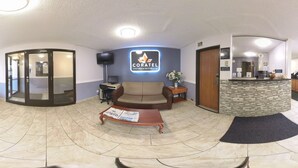 Una hall d'albergo con reception, un divano, un tavolino da caffè con quotidiani e un ingresso con porta in vetro.