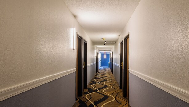 A hotel hallway with a patterned carpet, white walls, and doors on both sides.