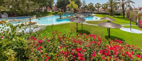 A resort pool area with multiple pools, surrounded by well-maintained lawns and tropical plants.