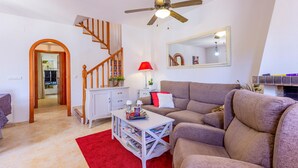 Ein Wohnzimmer mit Treppe, Deckenventilator, rotem Teppich, weißem Couchtisch mit Zeitschriften und einem großen Spiegel an der Wand.