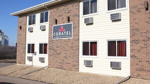 Un hotel con un letrero que dice "CORATEL INN & SUITES". Cuenta con fachada de ladrillo, múltiples ventanas y unidades de aire acondicionado.