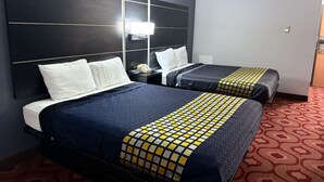 Una habitación de hotel con dos camas, un cabecero grande, una mesita de noche con una lámpara y una alfombra estampada.