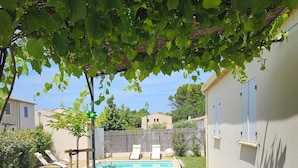 A patio with a glass table and chairs, a pool, and a pergola with green leaves. - Villa des Baumes (Beaumettes)
