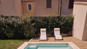 A rectangular swimming pool with clear water, surrounded by a pebble bed, two lounge chairs, and a hedge. - Villa des Baumes (Beaumettes)