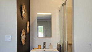A modern bathroom with a wooden vanity, a glass shower enclosure, and decorative wall art. - Villa des Baumes (Beaumettes)