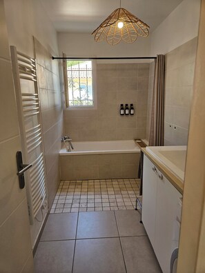 Une salle de bain avec une baignoire, une douche, une fenêtre avec des barreaux et un porte-serviettes.