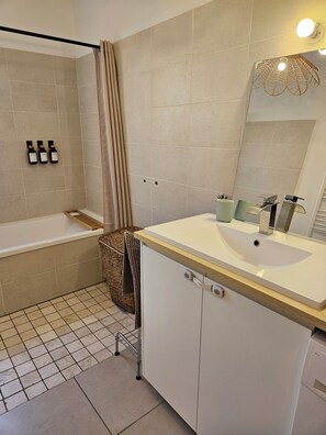 A bathroom with a bathtub, a sink, a mirror, and three bottles of shampoo. - Villa des Baumes (Beaumettes)