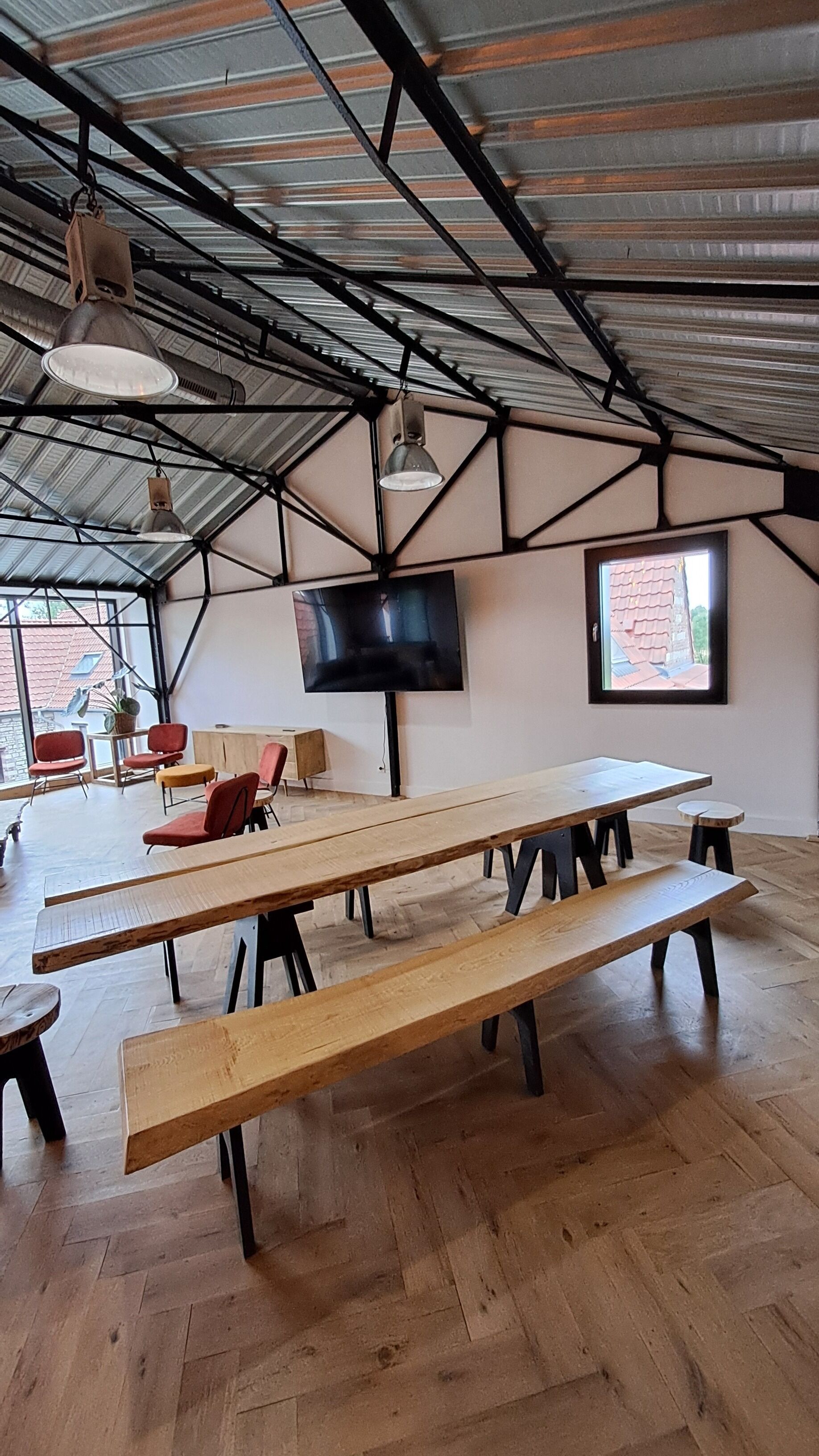 An indoor space with wooden benches, a TV mounted on the wall, and a large window with a view of buildings outside.