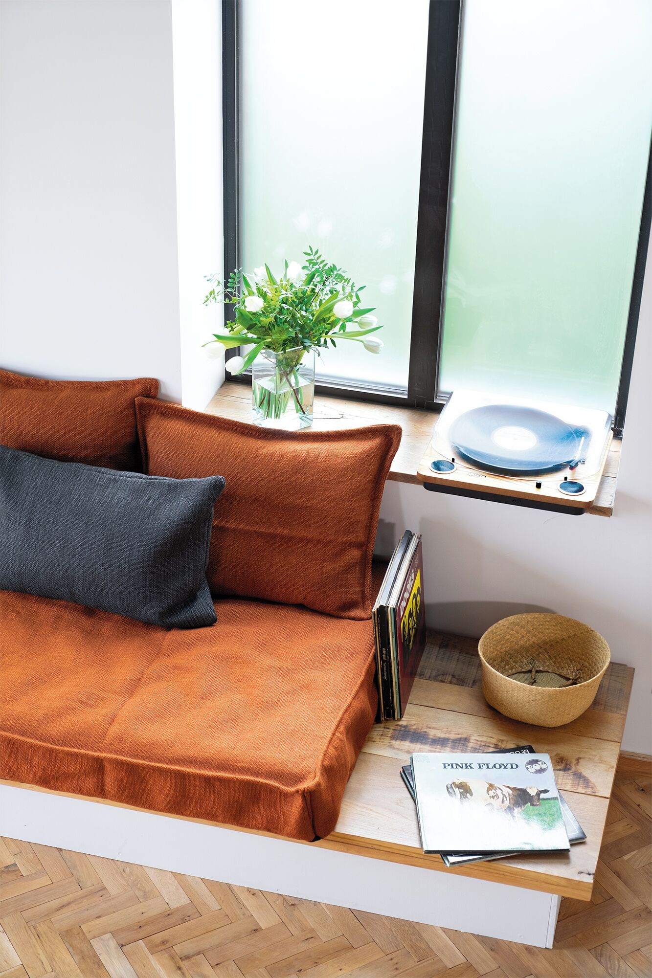 A modern living room with a brown sofa, a small table with a plant, a basket, and a magazine.