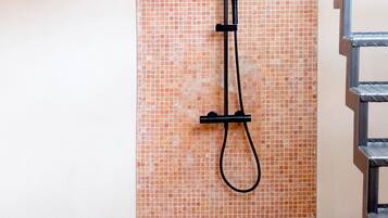 A shower area with a tiled wall, a metal handrail, and potted plants.