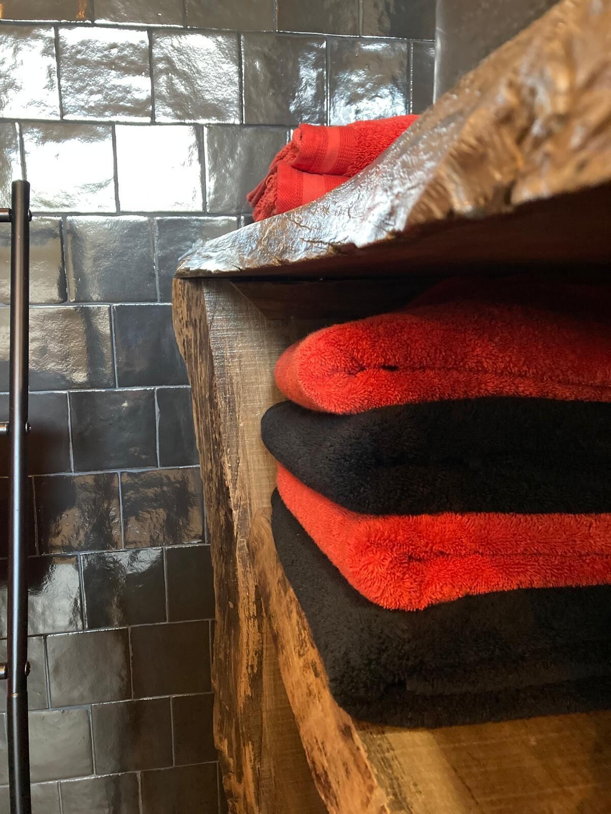 Een stapel rode en zwarte handdoeken op een houten ondergrond, achter een betegelde muur.