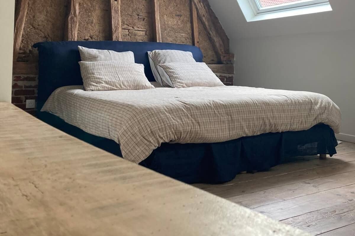 A bedroom with a sloped ceiling, a large window, and a bed with a blue headboard and white bedding.