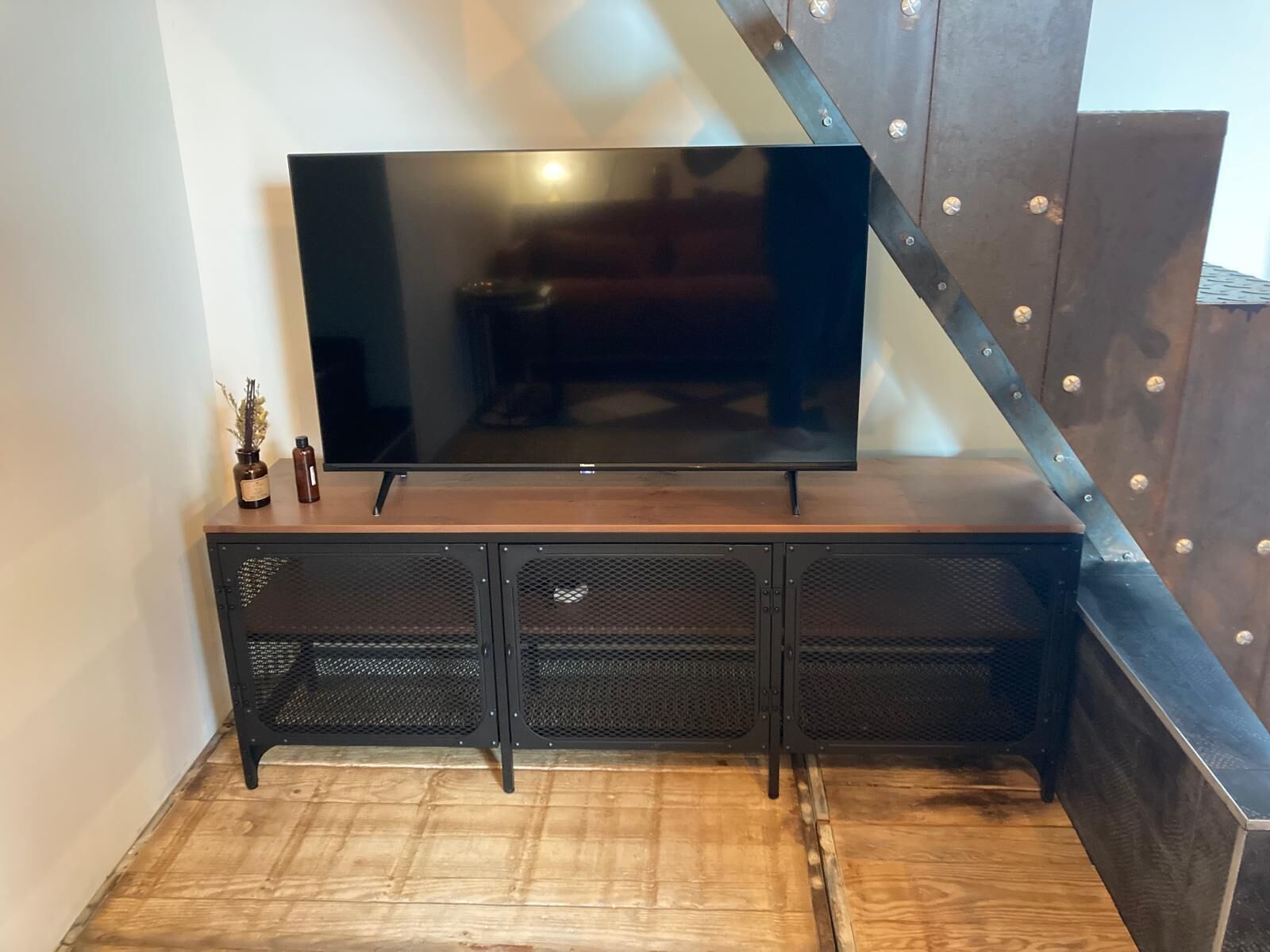A flat-screen TV on a wooden TV stand with mesh storage compartments.