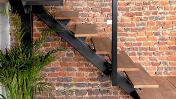 Un escalier avec un mur en briques en arrière-plan, une plante en pot et un sac à main posé sur le sol.