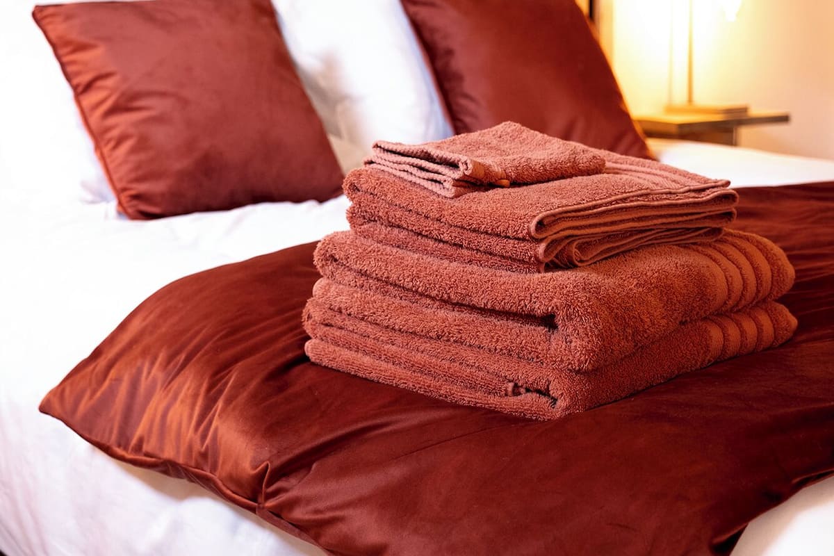 A neatly made bed with a stack of folded towels, white and brown bedding, and a wooden slat headboard.