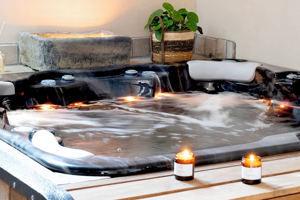 A hot tub with two candles and a plant on a wooden bench.