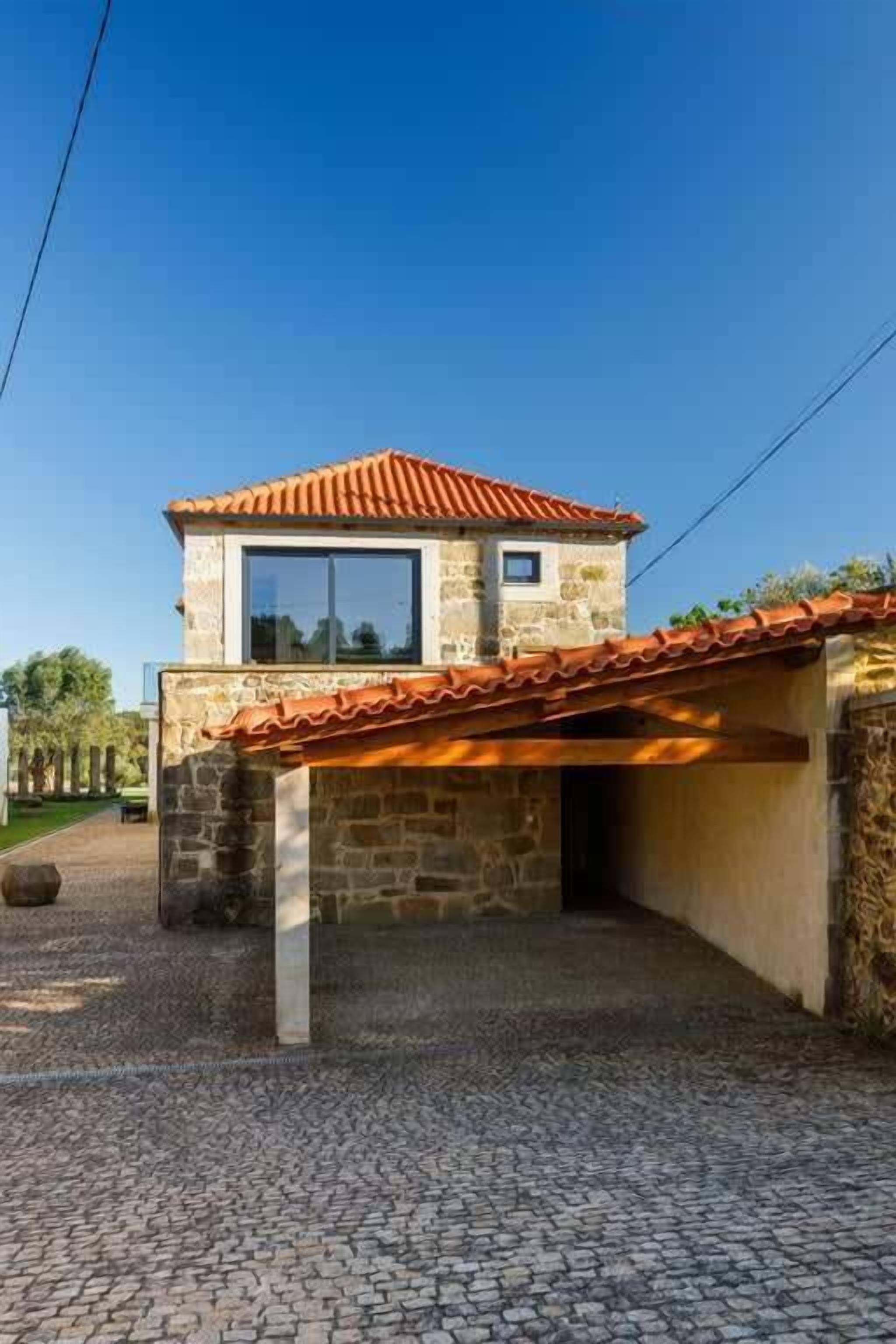 Un bâtiment en pierre avec un toit en tuiles, une fenêtre et une zone d’entrée pavée.