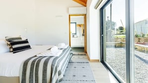Un dormitorio con cama, almohadas, una colcha a rayas, un tapete y un ventanal con vistas a un jardín.