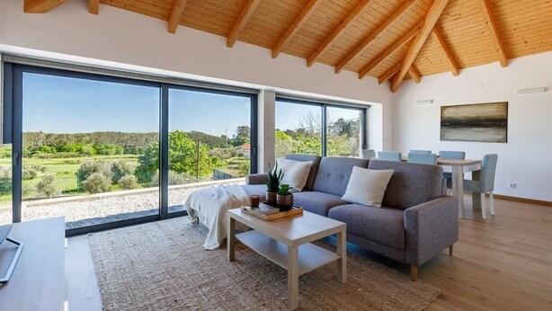 Amplia sala de estar con un ventanal, techo de madera, un sofá, una mesa de centro y un comedor.