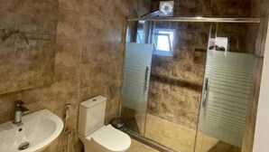 Kylpyhuone, jossa on kylpyamme, wc ja lasiseinällä varustettu suihkukaappi.