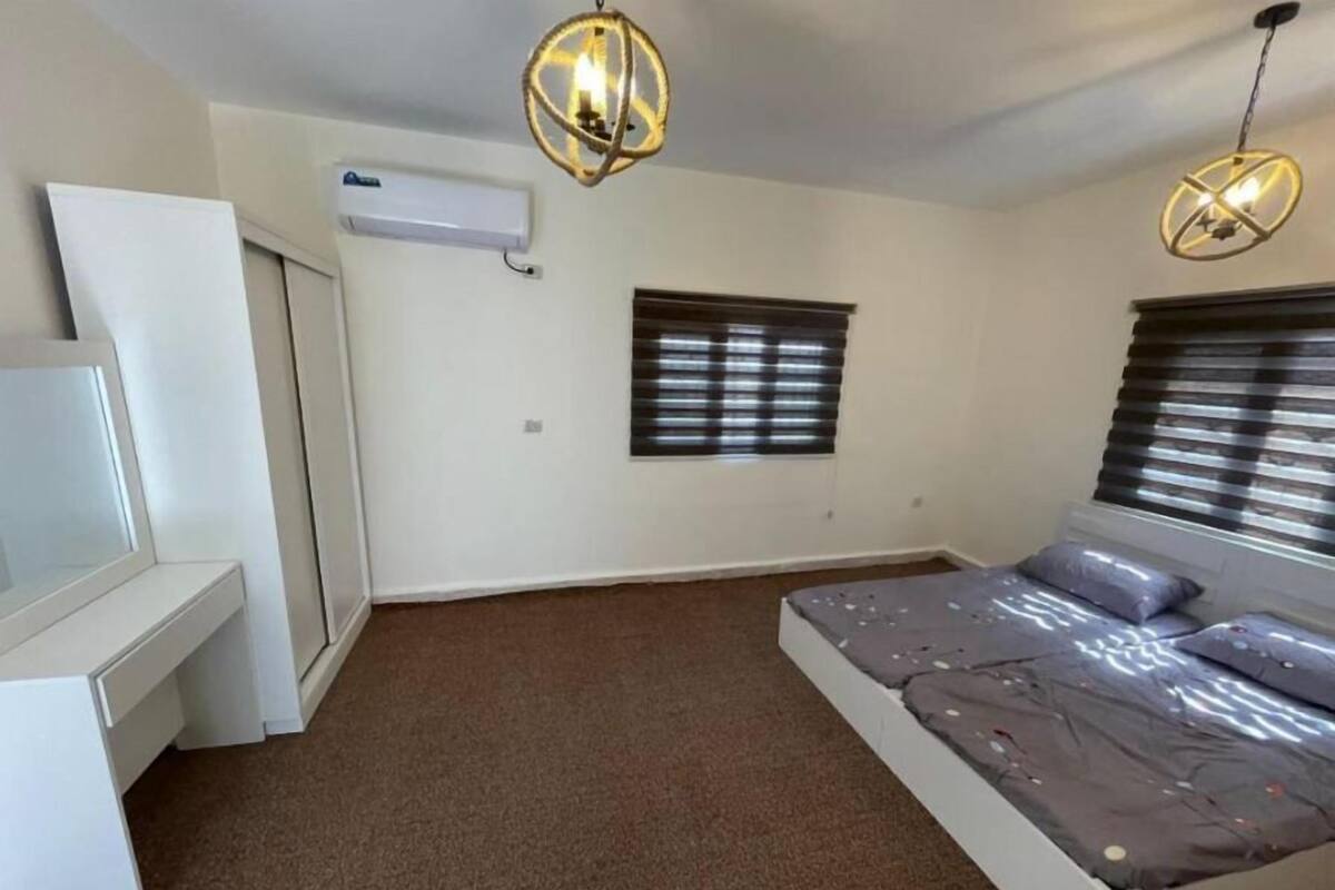 Ein Schlafzimmer mit einem Bett, zwei Fenstern mit Jalousien, einem Deckenventilator und einer Klimaanlage.