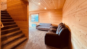 A log cabin interior with a staircase, a gray sofa, and a leather couch. - 12 miles from Yellowstone with incredible views - Grizzly Lodge (Island Park)