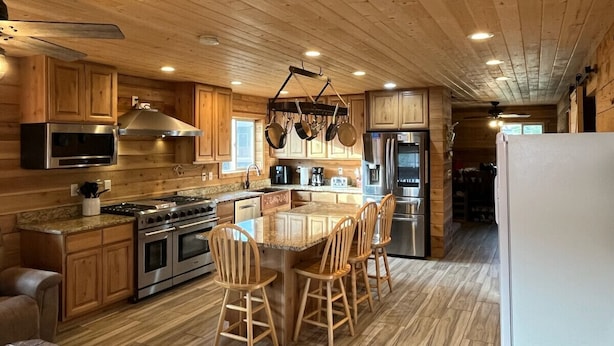 A spacious kitchen with wooden cabinets, a large island with chairs, stainless steel appliances, and a ceiling fan. - 12 miles from Yellowstone with incredible views - Grizzly Lodge (Island Park)