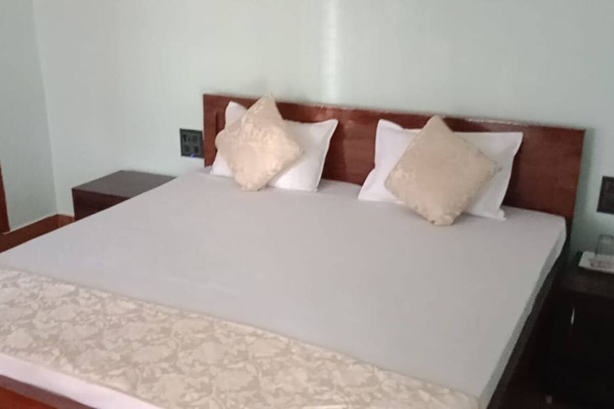 Un lit bien fait, recouvert d’une couvre-lit à motifs, deux tables de chevet avec une petite table sur chacune, et une tête de lit en bois.