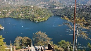Une vue panoramique d’un lac entouré d’une forêt dense et de petits bâtiments, avec une ligne de téléphérique visible au premier plan.