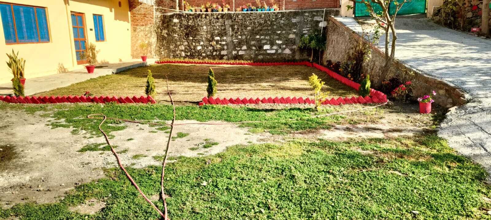 A courtyard with a stone wall, potted plants, and a red flower bed.