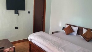 Une chambre à coucher avec un lit, des oreillers, un téléviseur fixé au mur et une table en bois.
