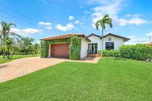 A two-story house with a garage, a well-maintained lawn, and palm trees. - Resort Like Amenities Close to Beach (Bonita Springs)