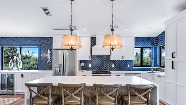 Een moderne keuken met een groot eiland, witte kastjes en een blauwe backsplash in herringbone patroon.