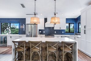 A modern kitchen with a central island, bar stools, and pendant lighting.
