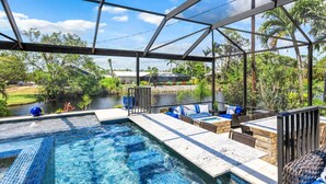 A pool area with a glass enclosure, seating, and a view of a river and greenery.