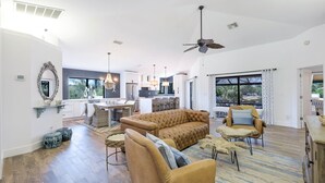 A spacious living area with a sofa, chairs, a dining table, and a kitchen in the background.
