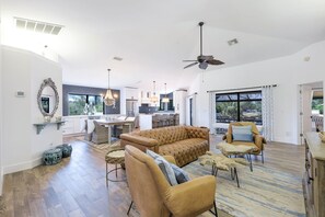 Een ruime woonkamer met een bank, stoelen, een eettafel en een keuken op de achtergrond.