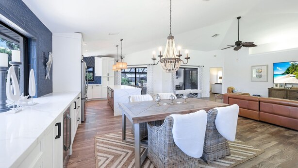 A modern kitchen with a dining area, a large chandelier, and a ceiling fan.