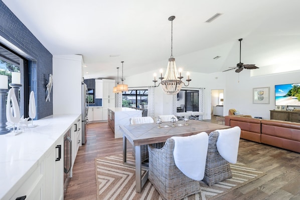 A modern kitchen with a dining area, a large chandelier, and a ceiling fan.