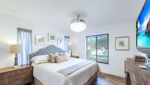 A bedroom with a large bed, a chandelier, a television, and framed pictures on the wall.