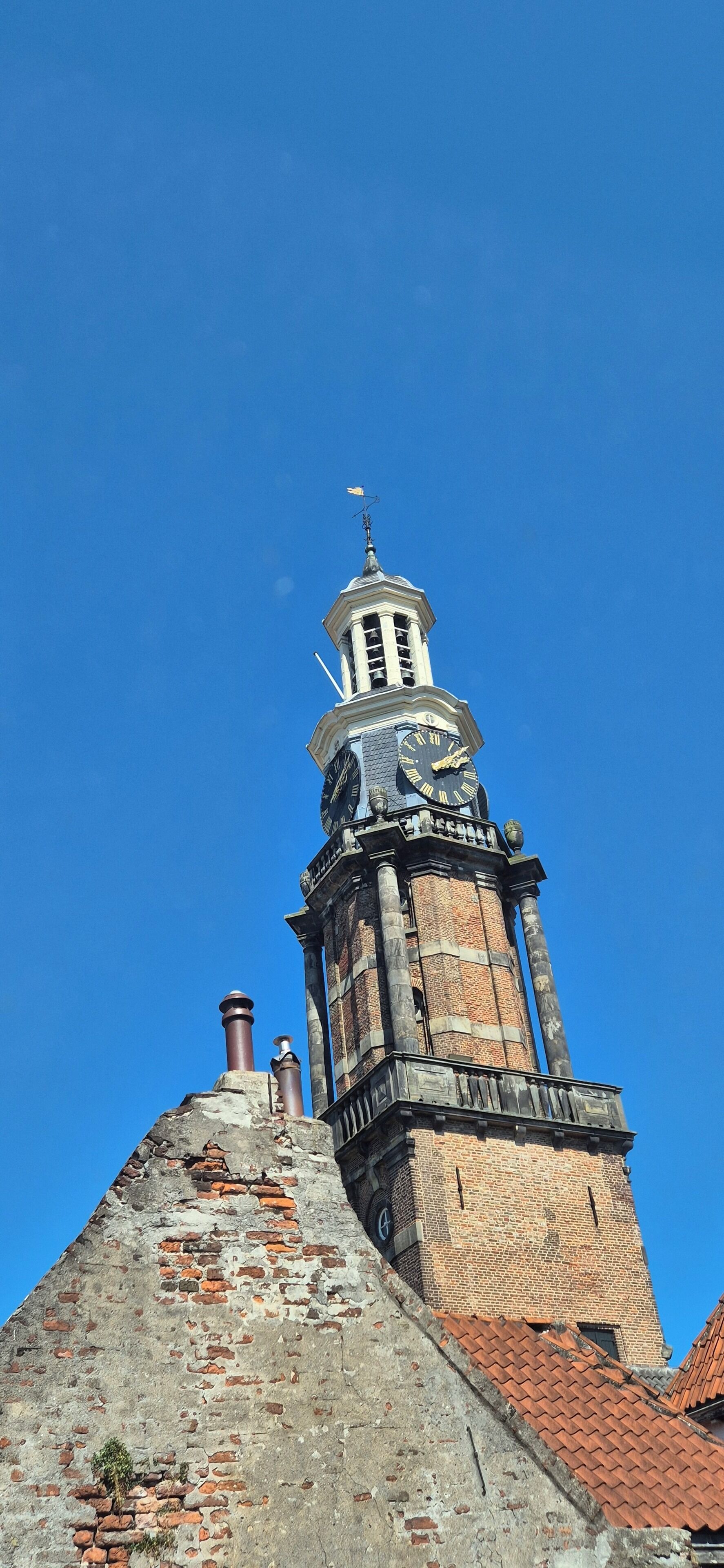 Un'alta torre in mattoni con un orologio e una veletta.
