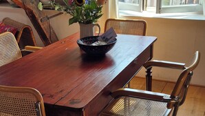 A dining area with a wooden table, four metal chairs, a vase with flowers, and a window with a view of a house. - Luxe Appartement in het Oude Centrum (Zutphen)