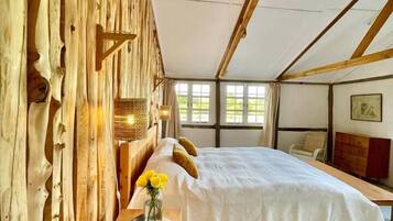 A room with a bed, a wooden desk, a vase with flowers, and a window.