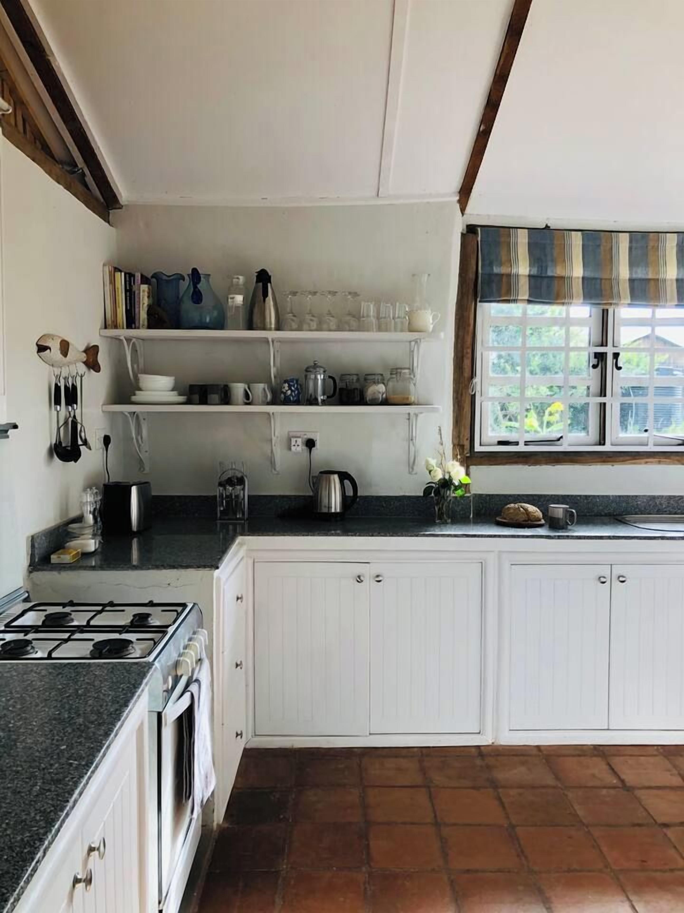 A kitchen with white cabinets, a stove, and a window with a striped valance.