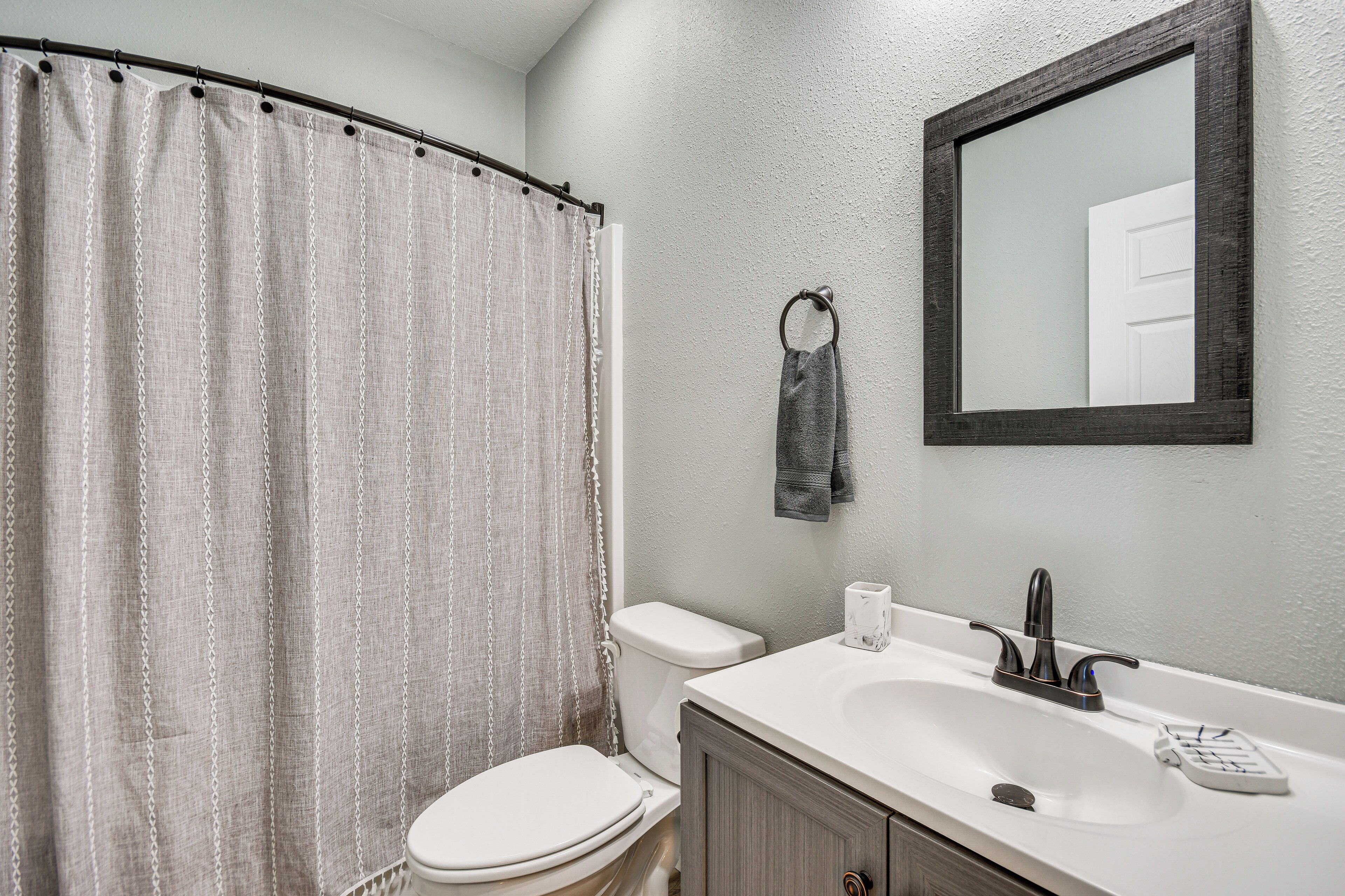 A bathroom with a shower curtain, toilet, sink, and a mirror.