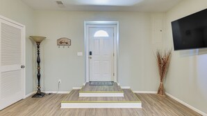 A hallway with a white door, a mounted TV, a floor lamp, and a decorative vase.