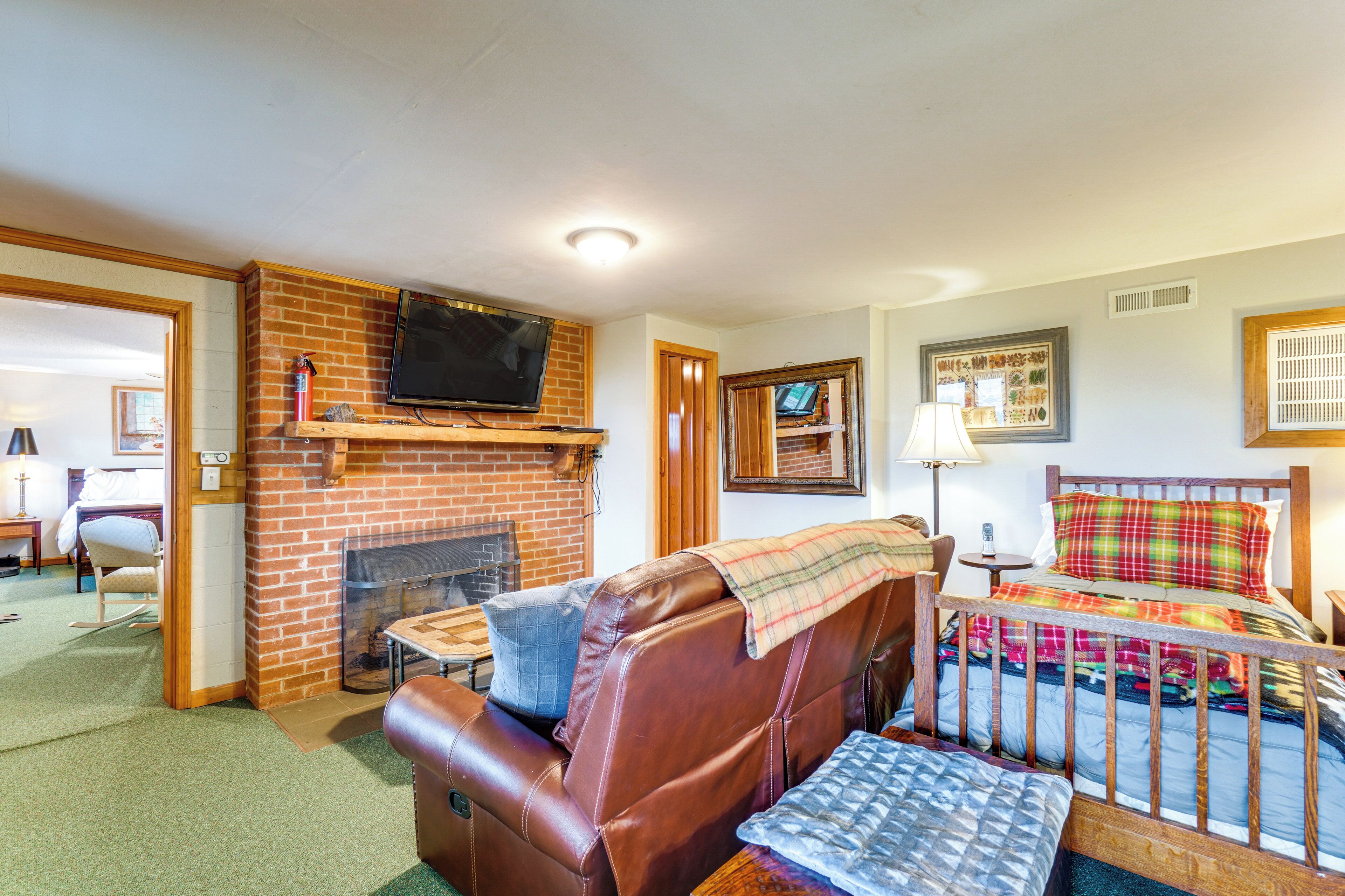 A hotel room with a brick fireplace, leather sofa, wooden bed, and a television mounted above the fireplace.