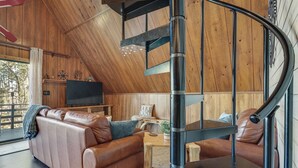 Um interior moderno com escada curva, sofá de couro, paredes de madeira e televisão.