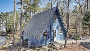 Uma cabana com telhado inclinado, um pequeno alpendre e um cais que se projeta sobre a água.